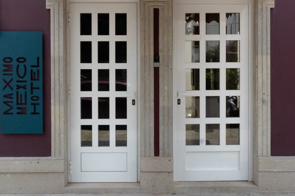 The hotel's entrance: two white glass-paned doors beneath the «Máximo México Hotel» sign on the wine-coloured facade