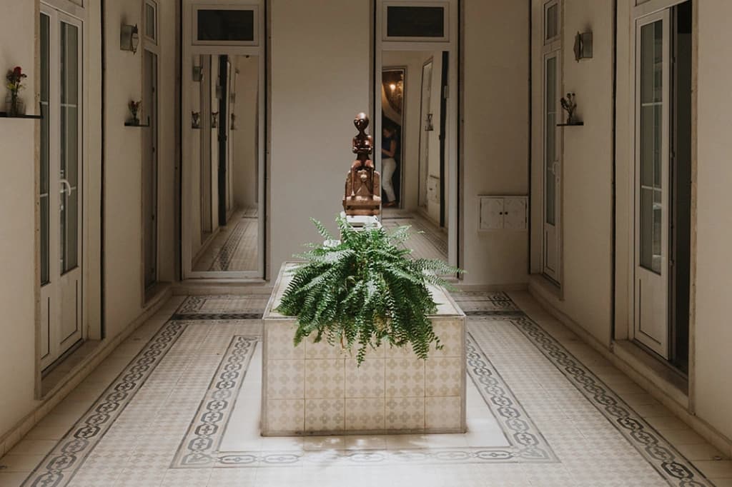 A hallway with mosaic tile flooring and a wooden sculpture among ferns, glass-paned doors on either side