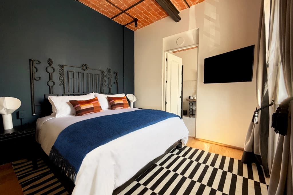 A room with a brick vaulted ceiling, a wrought-iron headboard against a dark blue wall and a blue throw at the foot of the bed
