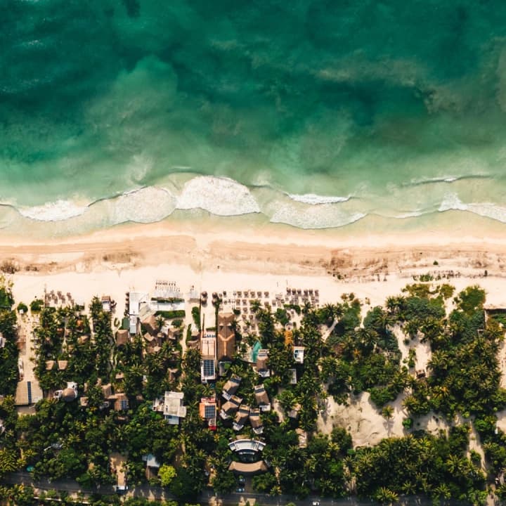An aerial view of the Tulum coastline, with palapa roofs among the jungle and the beach
