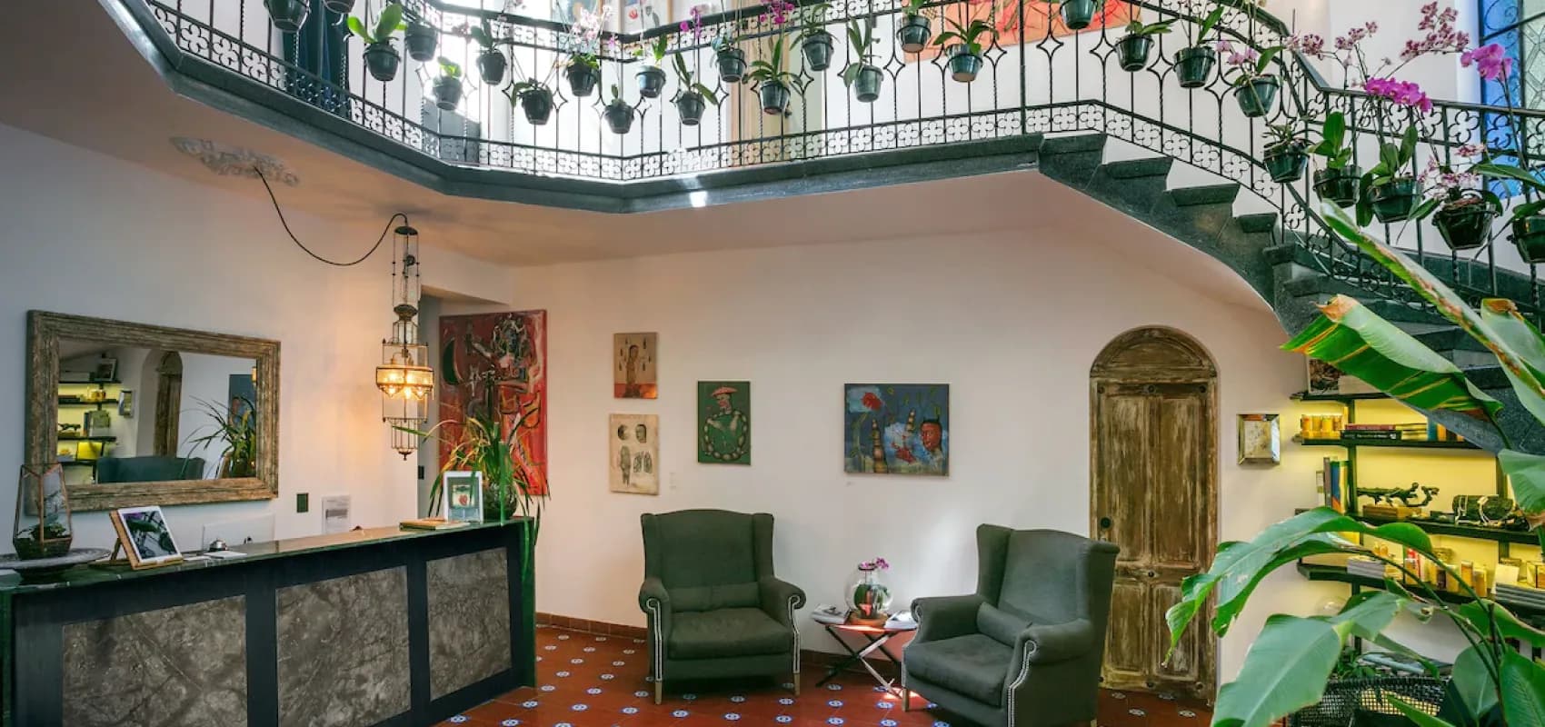 El lobby de Polanco visto de frente: la recepción, sillones verdes y la escalera de herrería con orquídeas colgantes al fondo