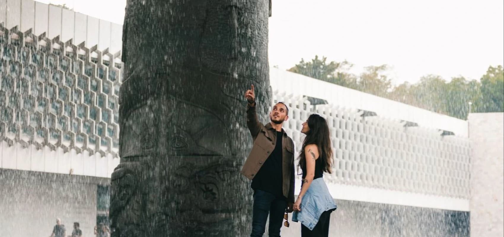 Una pareja bajo la lluvia de «El Paraguas», tocando el agua que cae de la columna tallada del Museo Nacional de Antropología